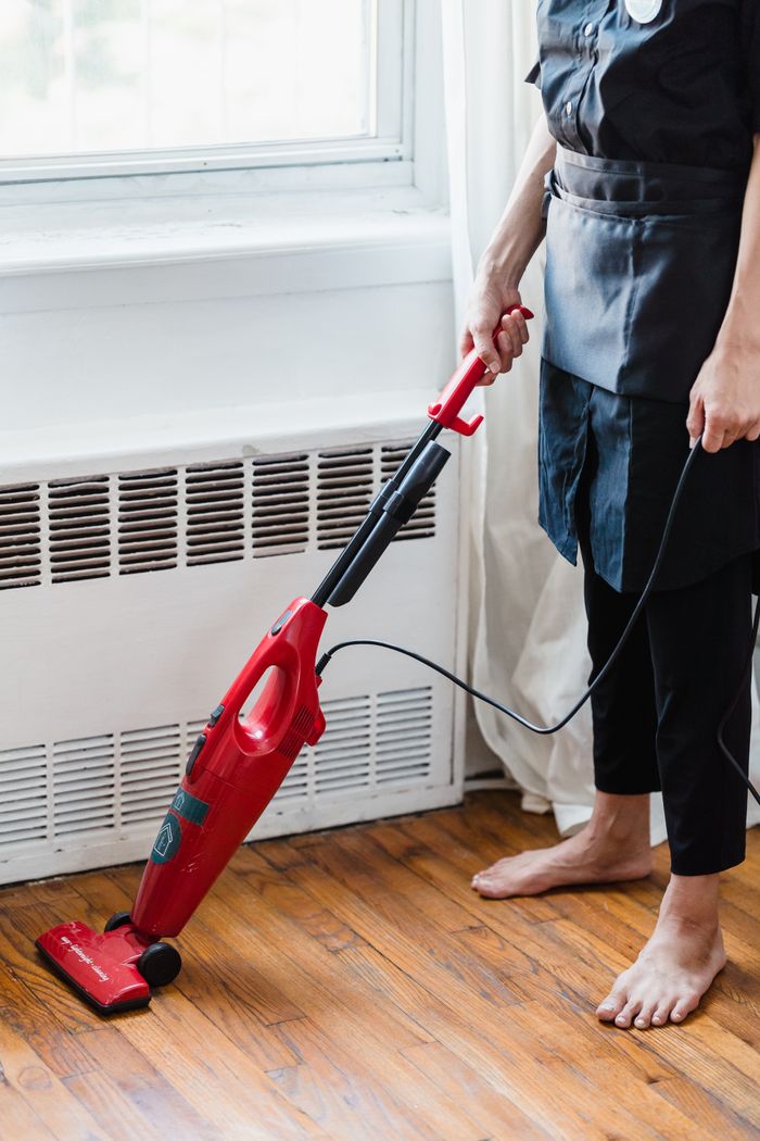 Person cleaning wooden floor with red vacuum cleaner in a well-lit room.